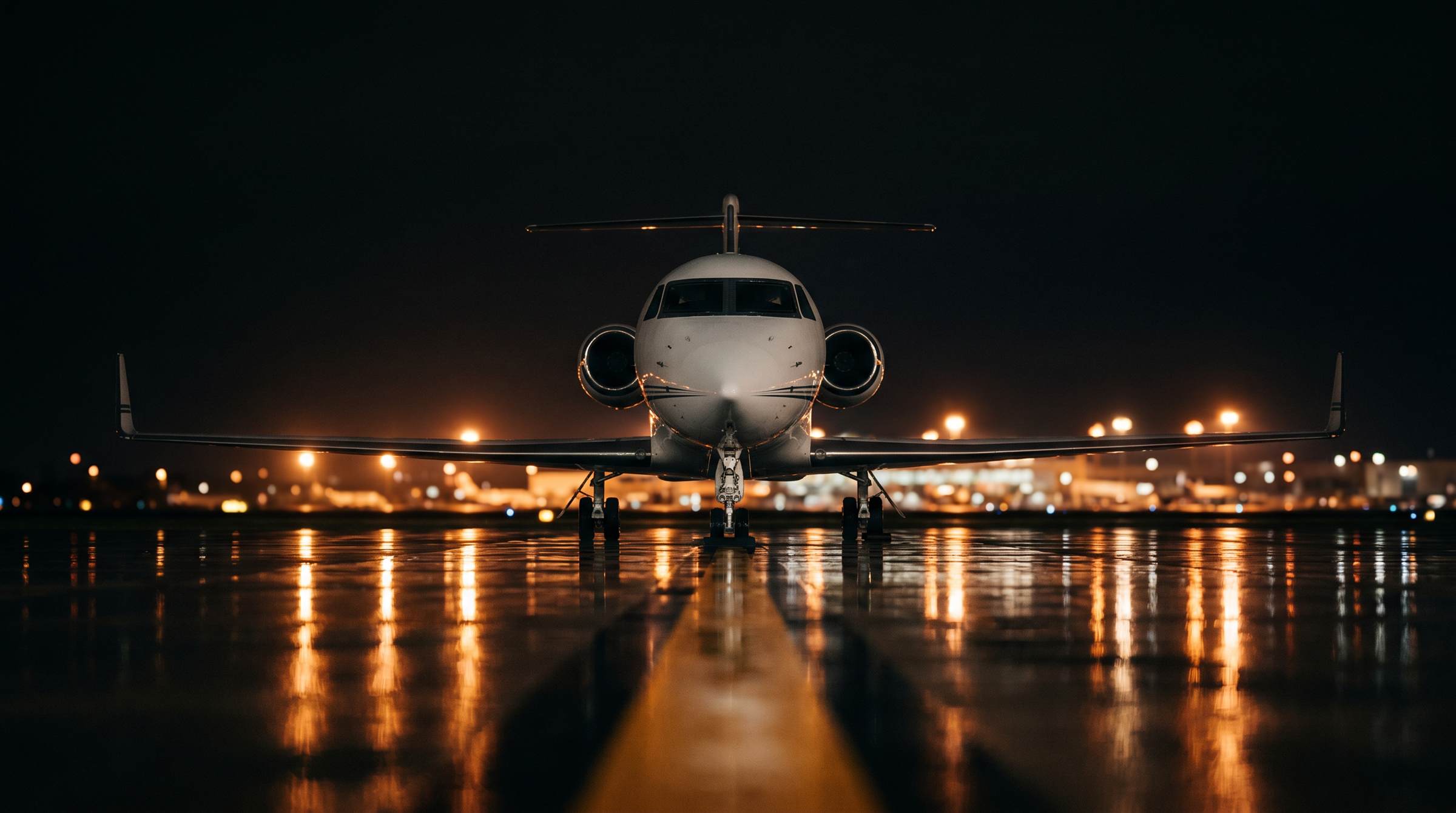 Private jet facing forward on a wet runway at night, surrounded by warm airport lights